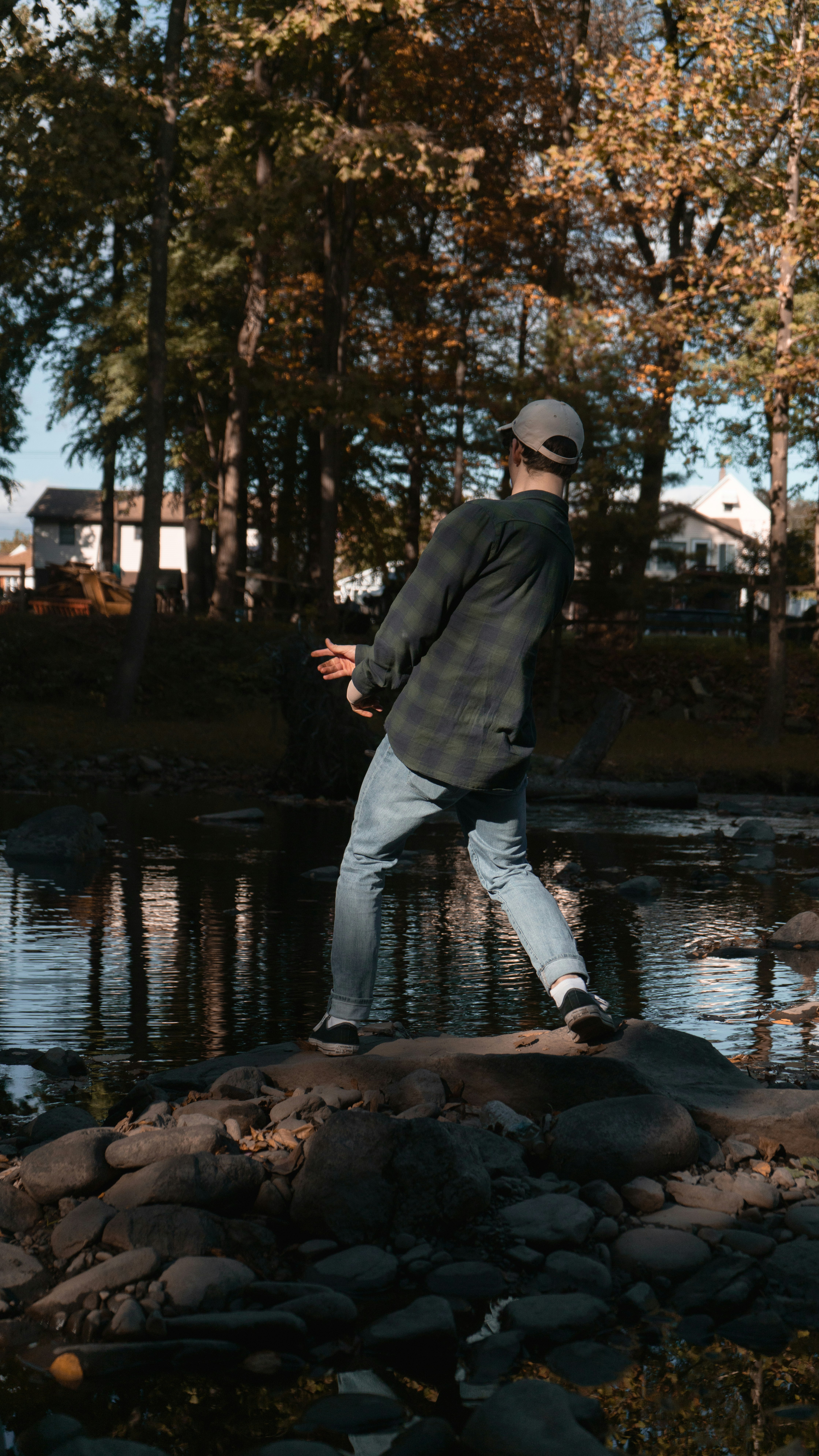 man in black jacket and gray pants standing on brown rock near river during daytime